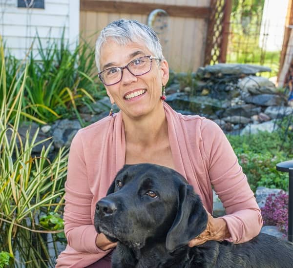 LeeAtherton Lee Atherton smiling outdoors with her black Labrador service dog, Shadow.
