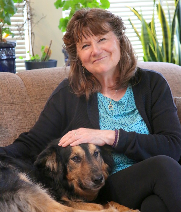 ElkeScholz Psychotherapist and author Elke Scholz smiling while seated on a sofa with her hand resting on her dog.